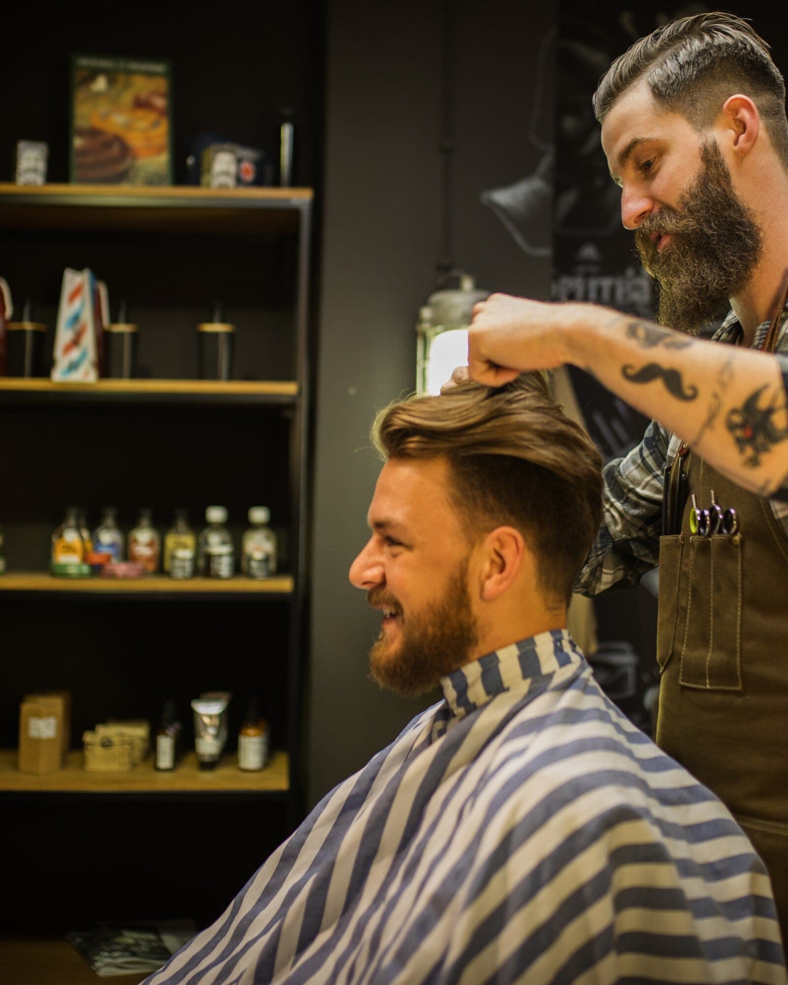 A barber styling a smiling client's hair in a barbershop
