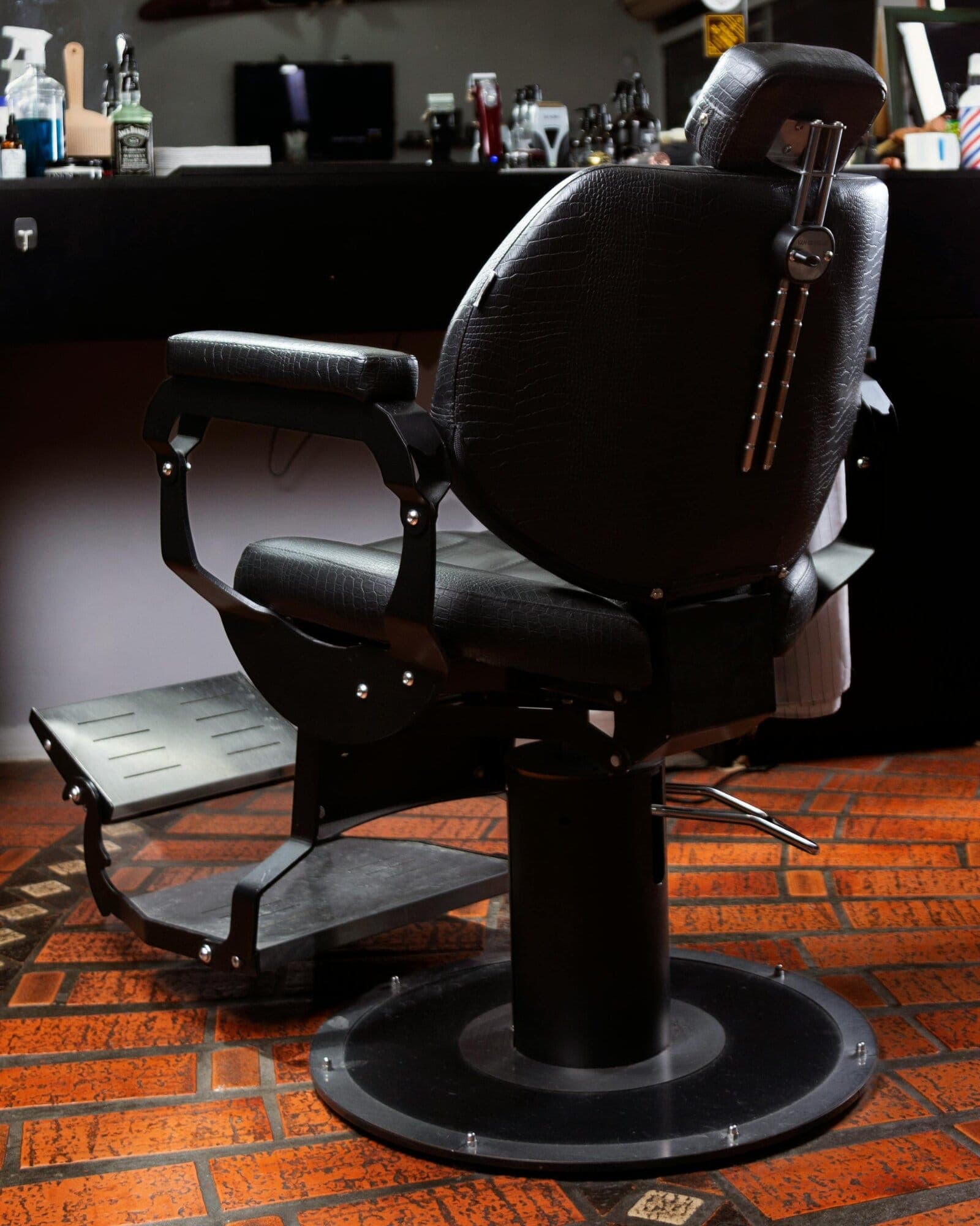 An empty black leather barber chair on a terracotta floor